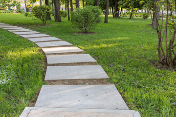 Wide stone path is in the park between trees