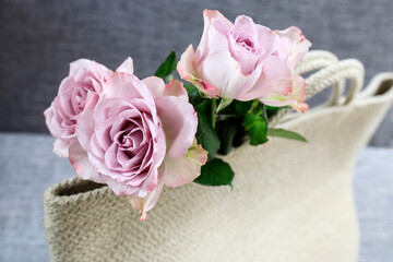 Three pale purple roses are visible from a white braided rope beach bag. Time to get together at sea.