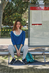 Thoughtful girl looking at camera. Girl sitting at bus stop wearing sportswear