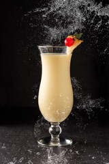 Pina colada cocktail splashing in glass on black background	