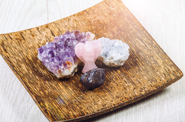 Group of gemstones on wooden tray in home interior. Rose quarz angel figurine, amethyst geode and...