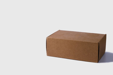 A closed cardboard box stands on a light background. Medium brown box with copy space