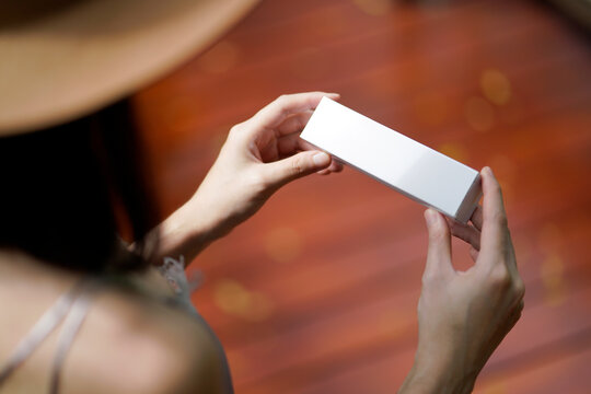 Stylish woman is holding and looking at white square box.