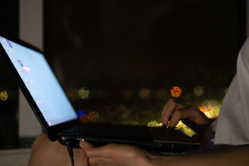 Young woman holds a laptop on her lap close - up at night near the window