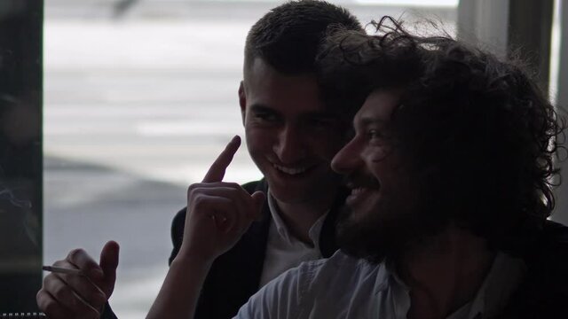 Male romanic gay couple in a cafe smoking a cigarette and cuddling, romantic lgbt couple concept