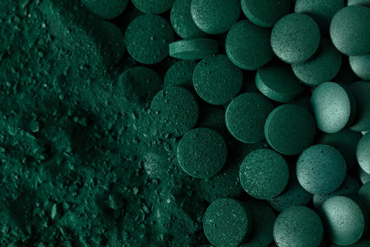 Green spirulina algae tablets and powder nutritional supplement macro close up top view.