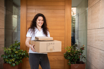 Woman with a couple of packages in her hands in front of her front door smiling.  delivery concept