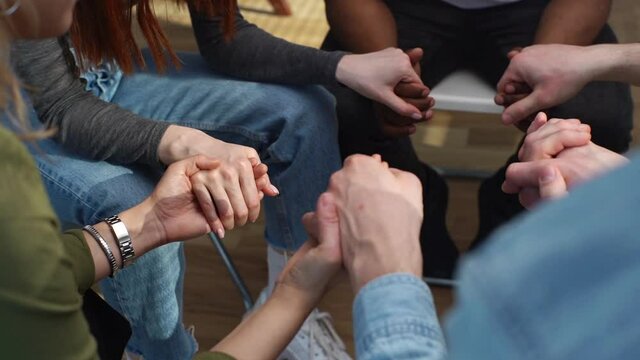 Close-up top view of hands unrecognizable multiethnic diverse men and women sitting in circle support each other, holding hands during group interpersonal therapy session. Tracking shot in slow motion