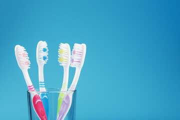 Colorful toothbrushes in a glass on a blue background.
