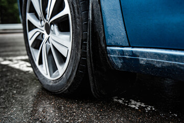 Car mudgaurd, mudflap on front wheel of blue car parking on wet asphalt. - obrazy, fototapety, plakaty
