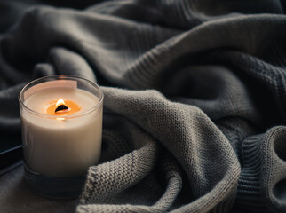 Burning candle in glass with wooden wick, handmade natural wax candle with knitted blanket