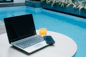 Laptop Mobile Phone and glass of orange at poolside