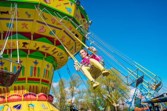 A little girl child in bright clothes rides on a carousel in an amusement park. Kazan, Russia - 8 May 2021