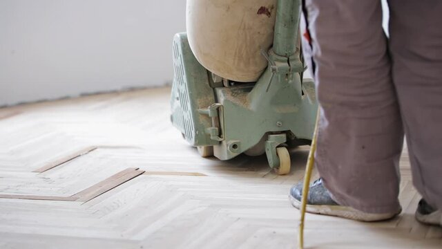 Repairman restoring parquet with a sanding machine.