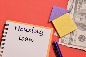 Top view of pen, money banknotes, toy house and notebook written with HOUSING LOAN. Real estate concept.