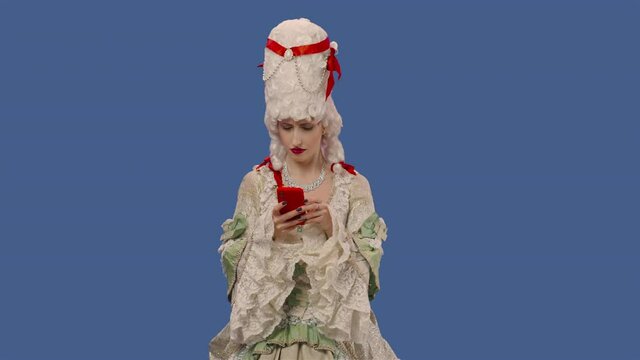 Portrait of courtier lady in white vintage lace dress and wig texting on her phone. Young woman posing in studio with blue screen background. Close up. Slow motion ready 59.94fps.
