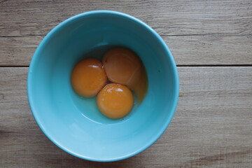 Three egg yolks are in a blue bowl, cooking food.