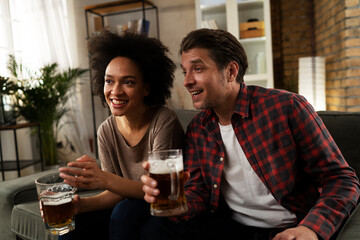 Boyfriend and girlfriend drinking beer at home. Happy couple watching sports game on tv.