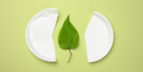 broken white plastic plate and green leaf on a green background. The concept of avoiding plastic
