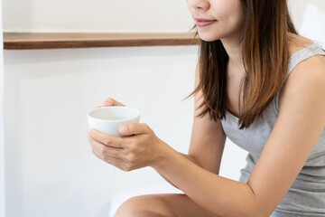 Close up of happy Asian girl sitting on bed holding a cup of coffee.