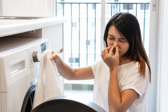 Young Asian woman looking at dirty smelly clothe out of washing machine in kitchen.