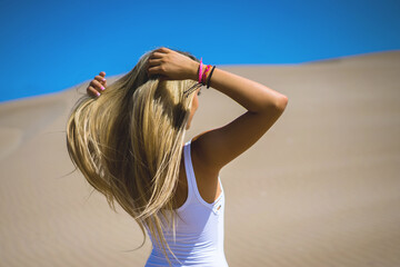 Chhica vestida de blanco peinandose en el desierto con ondas de arena mientras el viento sopla