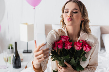 Woman with roses taking selfie on smartphone and pouting lips at home