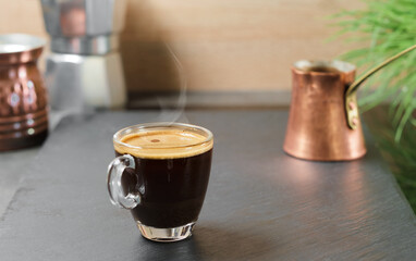 Coffee break. Fresh espresso steam rises in a glass goblet above the cup, selective focus. Strong...
