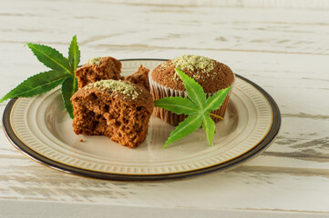 Healthy and tasty vegan and gluten free muffins in a row topped with hemp seeds on a marble table. Marijuana cupcake muffins with cannabis leaves