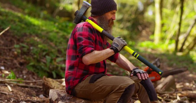 Man holding heavy axe taking a break from chopping or cutting wood trunks .