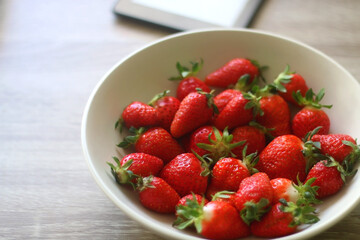 Bowl of fresh strawberries and tablet on wooden table. Selective focus.