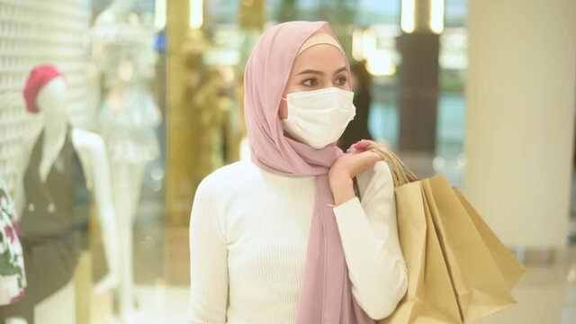 Young muslim woman wearing protective mask in shopping mall, shopping under Covid-19 pandemic concept.