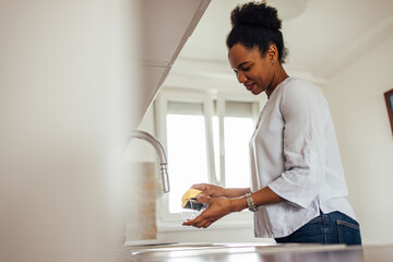 Black woman, washing glass with detergent and sponge.