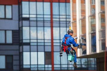 Professional climber rope access worker cleaning the windows on the high rise building, industrial mountaineers washing the glass facade of a modern building, working at heights