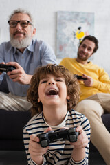 KYIV, UKRAINE - APRIL 12, 2021: Excited kid playing video game near blurred parents © LIGHTFIELD STUDIOS