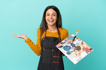 Young artist caucasian woman holding a palette isolated on blue background with shocked facial expression