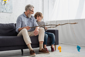 Cheerful grandfather and kid playing toy fishing