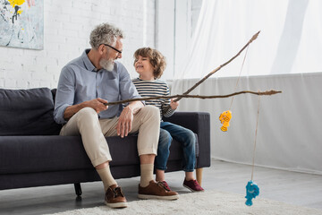 Smiling grandfather and boy looking at each other while playing toy fishing