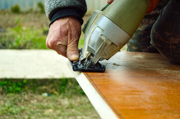a carpenter saws off a piece of chipboard with an electric hand jigsaw - obrazy, fototapety, plakaty