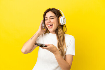 Caucasian woman isolated on yellow background listening music with a mobile and singing