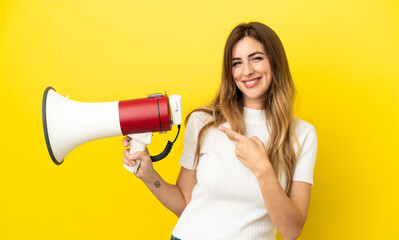 Caucasian woman isolated on yellow background holding a megaphone and pointing side