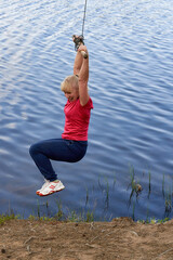 Middle aged woman in sportswear hanging on a stick with a rope above the water