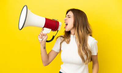 Caucasian woman isolated on yellow background shouting through a megaphone to announce something in...