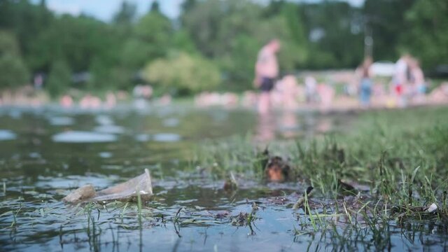 A city beach and a dirty glass in the water. Environmental pollution. Dirty water. People bathe in the background