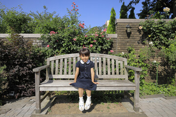 バラ園のベンチに座る幼児(5歳児) - obrazy, fototapety, plakaty