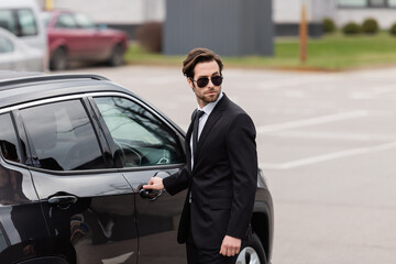 bodyguard in sunglasses with security earpiece opening door of modern auto