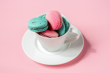 Colorful macaroons in a white cup on a pink background. Sweet dessert for coffee and tea. Idea for postcards