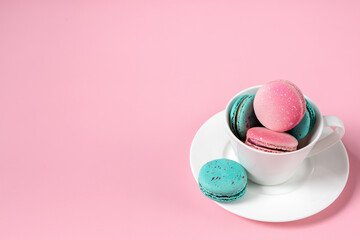 Colorful macaroons in a white cup on a pink background with a space for text . Sweet dessert for coffee and tea. Idea for postcards