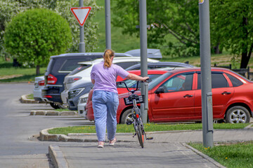A girl walks next to her bike on the city sidewalk