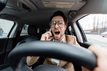 angry man talking on smartphone while driving car on blurred foreground